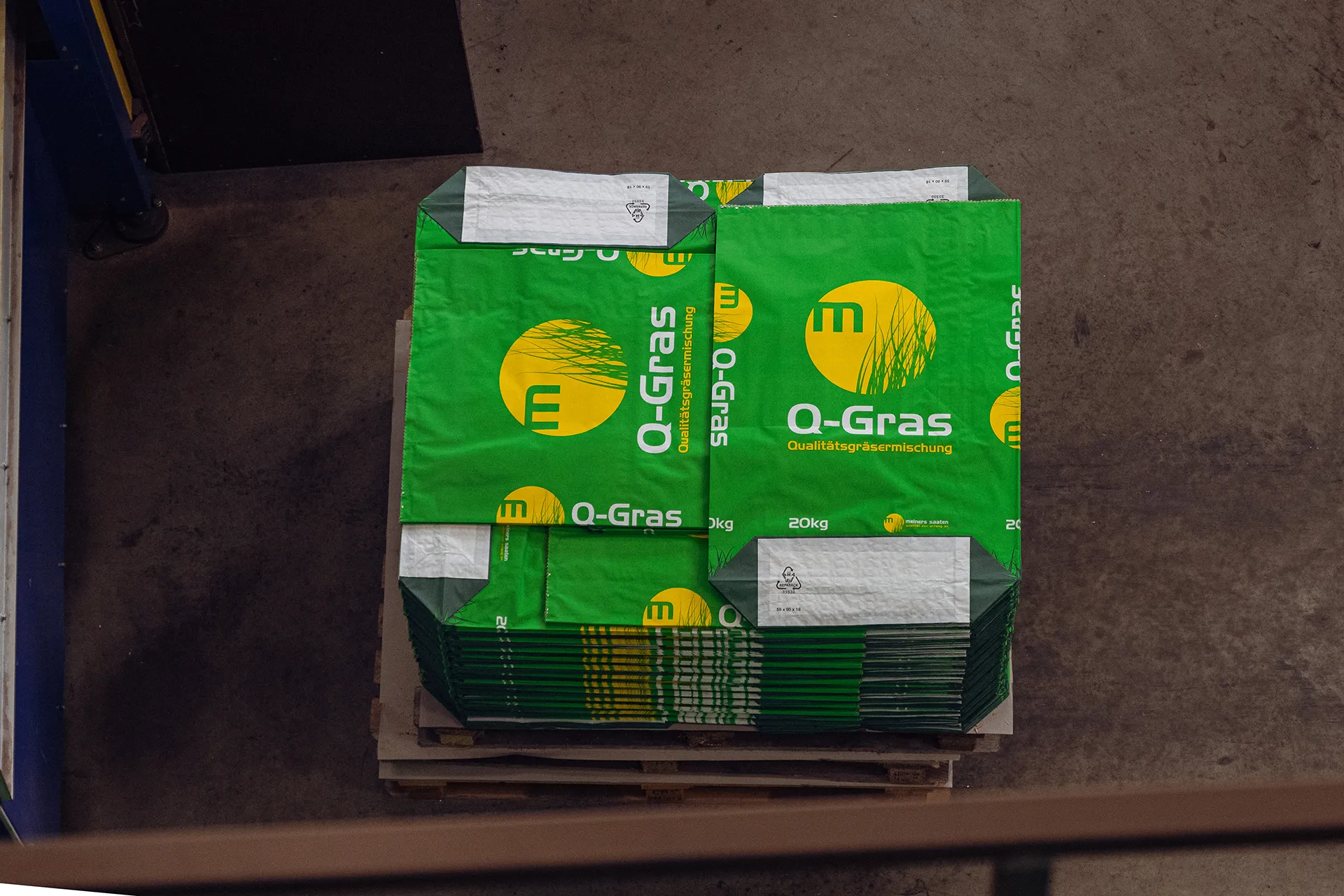 Verpackungsanlage Meiners Saaten mit grünen Q-Gras Säcken, automatisierte Produktion, moderne Fördertechnik, Saatgutverarbeitung.